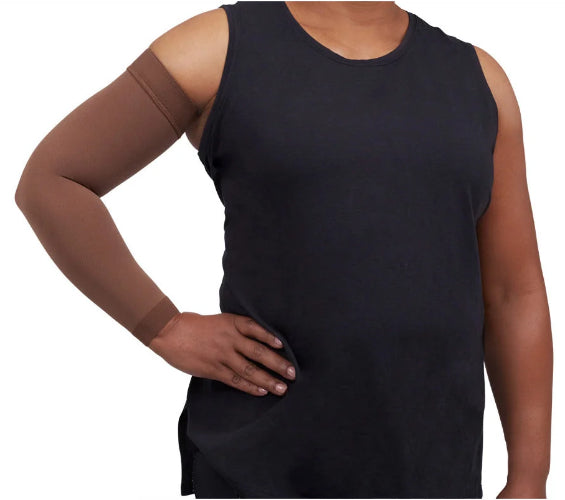 A person wearing a black sleeveless tank top and a Java colored Medi Comfort arm compression sleeve on one arm, shown against a plain white background.