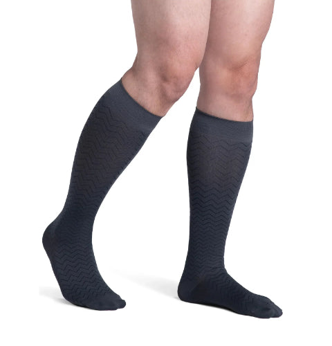 A male wearing his Sigvaris Microfiber Pattern 20-30 mmHg compression knee-high stocking with a graphite chevron design.