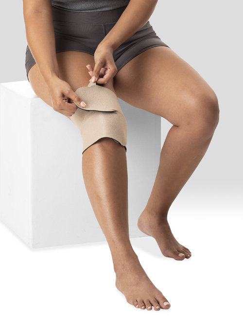 Lady sitting down putting her Juzo Velcro Compression Wrap for the Knee in the color Beige