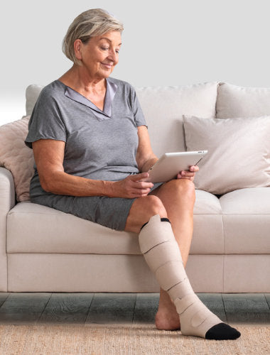 Lady sitting on couch wearing her Juzo Compression calf and foot wrap in the color beige.